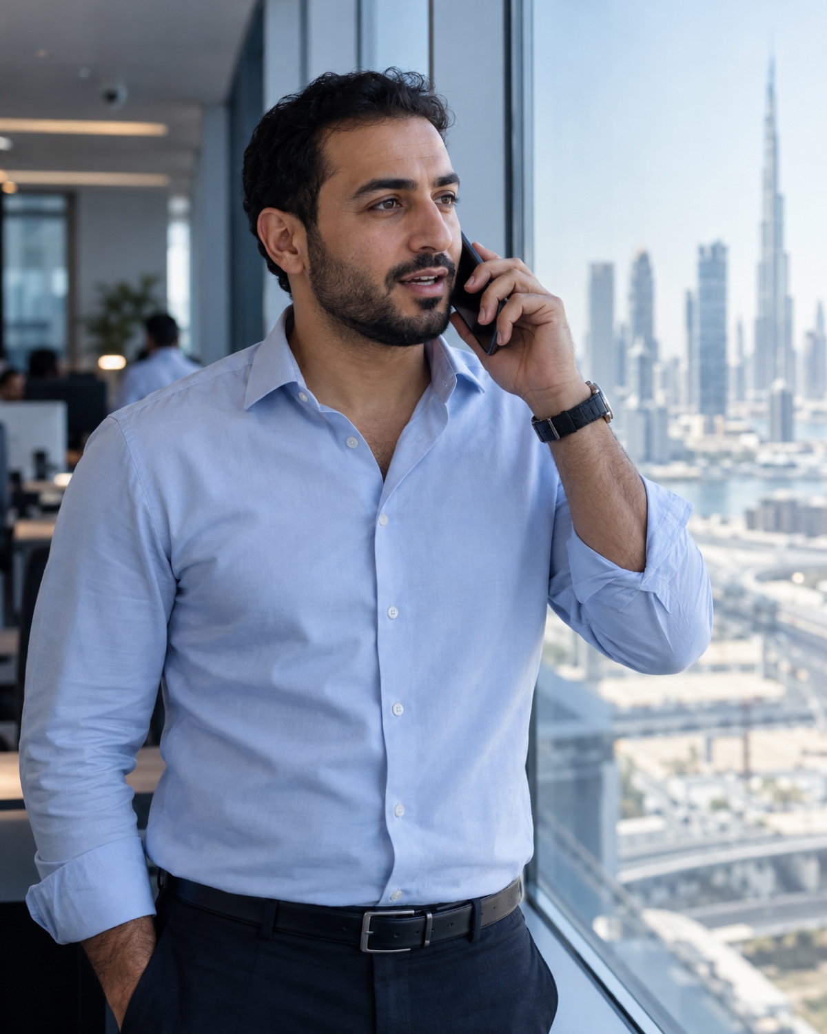 Support engineer in an open-collar shirt taking a call beside a Dubai office window